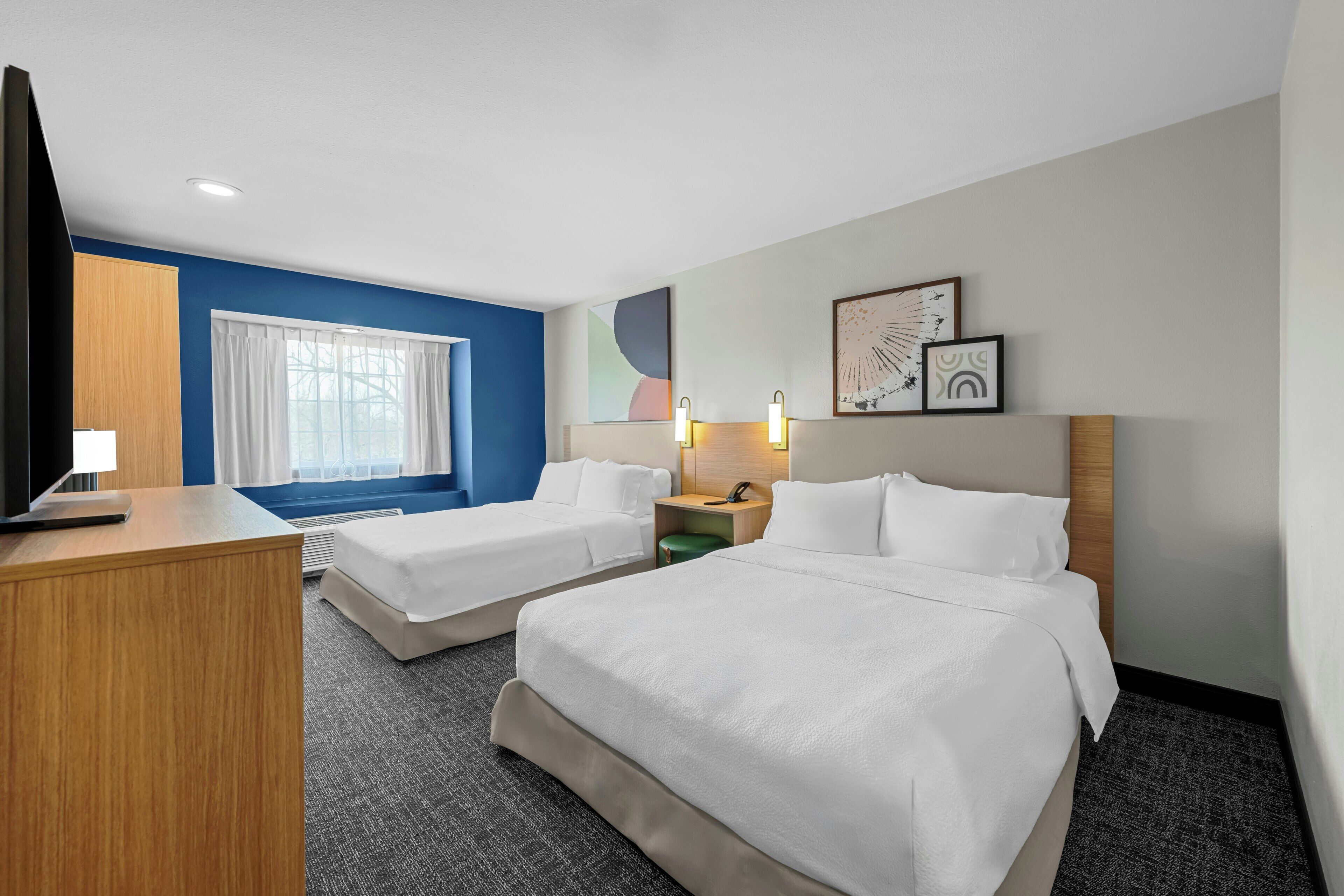 Une chambre d’hôtel avec deux lits, un bureau, une télévision et une fenêtre avec des rideaux.