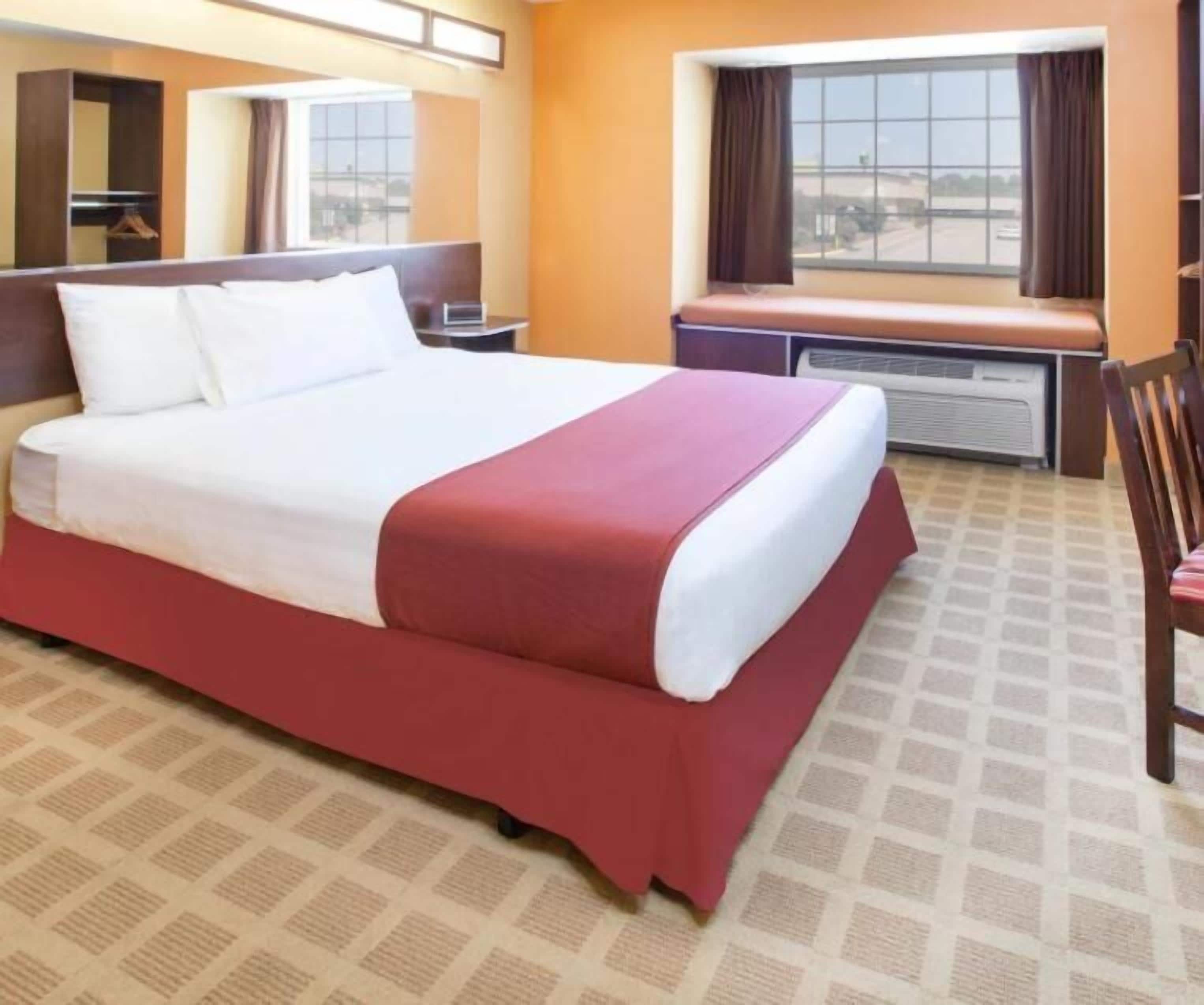 Une chambre d’hôtel avec un grand lit, une fenêtre avec des rideaux, un bureau et une chaise.