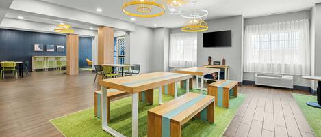 A modern hotel room with a dining area, wooden furniture, and a flat-screen TV.