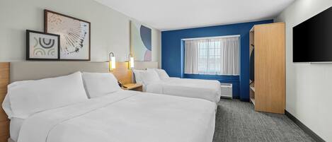 A hotel room with two beds, a TV, a wardrobe, and artwork on the walls.