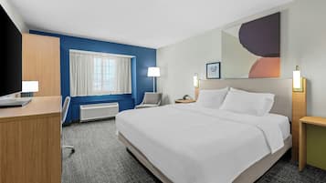 A hotel room with a bed, a desk, a chair, a nightstand, a lamp, and a window with curtains.