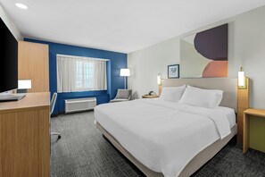 A hotel room with a bed, a desk, a chair, a nightstand, a lamp, and a window with curtains. - Spark by Hilton Stillwater (Stillwater)