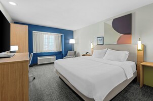 Habitación de hotel con cama, escritorio, silla, mesita de noche, lámpara y ventana con cortinas.