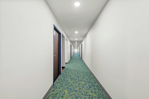 Un largo y estrecho pasillo de hotel con alfombra estampada y puertas a un lado.