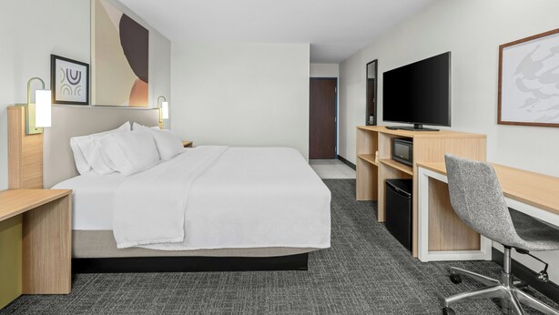 A hotel room with a bed, desk, chair, television, and artwork on the walls. - Spark by Hilton Stillwater (Stillwater)