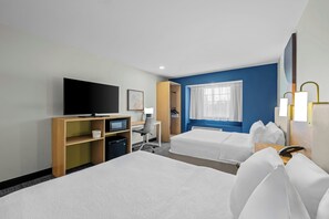 Una habitación de hotel con dos camas, un escritorio con una computadora, un televisor y una ventana con cortinas.