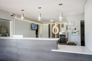 A reception area with a modern design, including a reception desk, pendant lighting, and a wall-mounted television. - Motel6 Topeka, KS - Northwest (Topeka)
