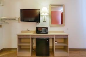 A hotel room with a flat-screen TV, a microwave, a refrigerator, a lamp, a mirror, and a wooden desk with shelves. - Motel6 Topeka, KS - Northwest (Topeka)
