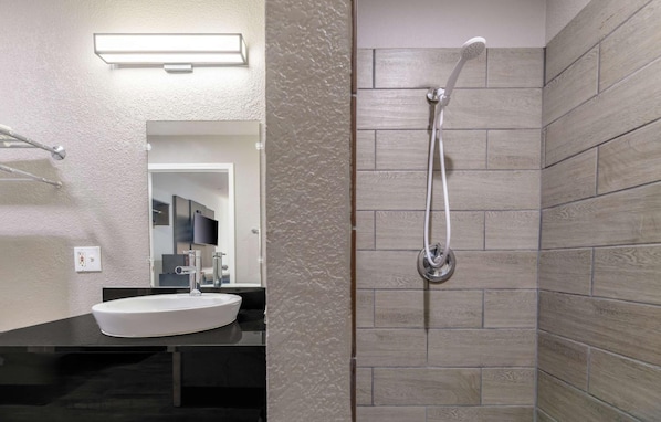 A bathroom with a white sink, a mirror, a shower with a handheld showerhead, and textured walls. - Motel6 Topeka, KS - Northwest (Topeka)