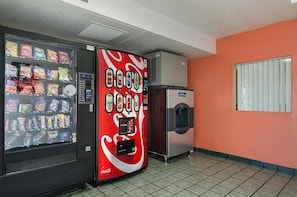 A vending machine with snacks and Coca-Cola, a water dispenser, and a window with blinds. - Motel6 Topeka, KS - Northwest (Topeka)