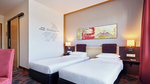 A hotel room with two single beds, a red chair, a wall with a text and abstract art, and a patterned carpet. - Lindner Hotel Nurburgring Motorsport, Part of JDV by Hyatt (Nuerburg)
