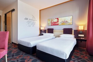 A hotel room with two single beds, a red chair, a wall with a text and abstract art, and a patterned carpet. - Lindner Hotel Nurburgring Motorsport, Part of JDV by Hyatt (Nuerburg)