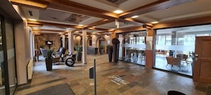 A hotel lobby with a stone wall, wooden beams, a reception desk, and a seating area with chairs and tables. - Lindner Hotel Nurburgring Motorsport, Part of JDV by Hyatt (Nuerburg)