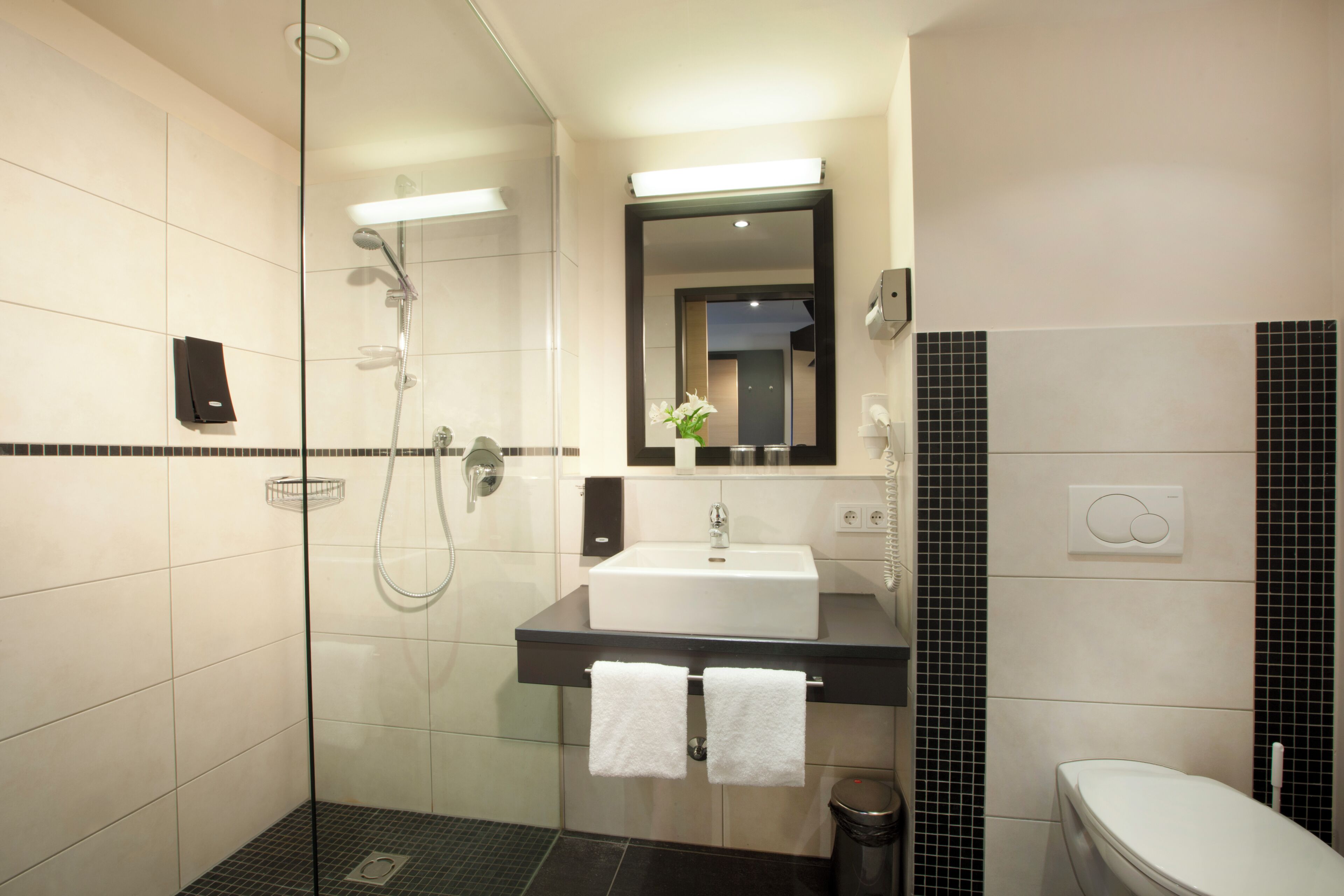 Un bagno moderno con cabina doccia in vetro, lavandino bianco su piano di appoggio nero e un water.
