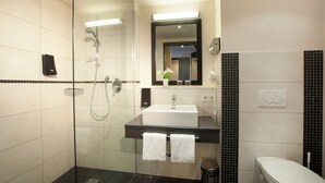 A modern bathroom with a glass-enclosed shower, a white sink with a black countertop, and a toilet. - Lindner Hotel Nurburgring Motorsport, Part of JDV by Hyatt (Nuerburg)