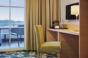Habitación de hotel con un ventanal grande, una silla, un escritorio con lámpara y vistas al exterior.
