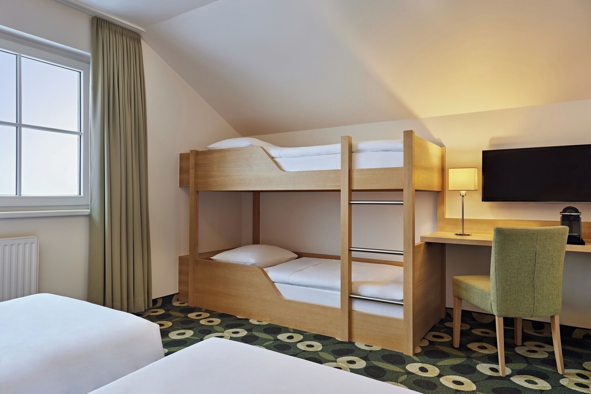 A bunk bed with a desk and chair, a television, and a window with curtains.
