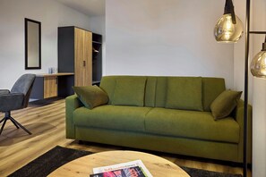 A modern living room with a green sofa, a wooden coffee table, and a magazine on it. - Lindner Hotel Nurburgring Motorsport, Part of JDV by Hyatt (Nuerburg)