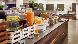Um buffet de café da manhã com diversos sucos, uma máquina de café e uma seleção de doces.