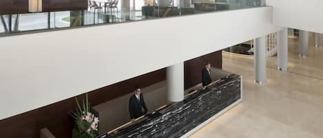 Un moderno vestíbulo de hotel con mostrador de recepción, zona de estar y barandilla de vidrio con vistas al interior.