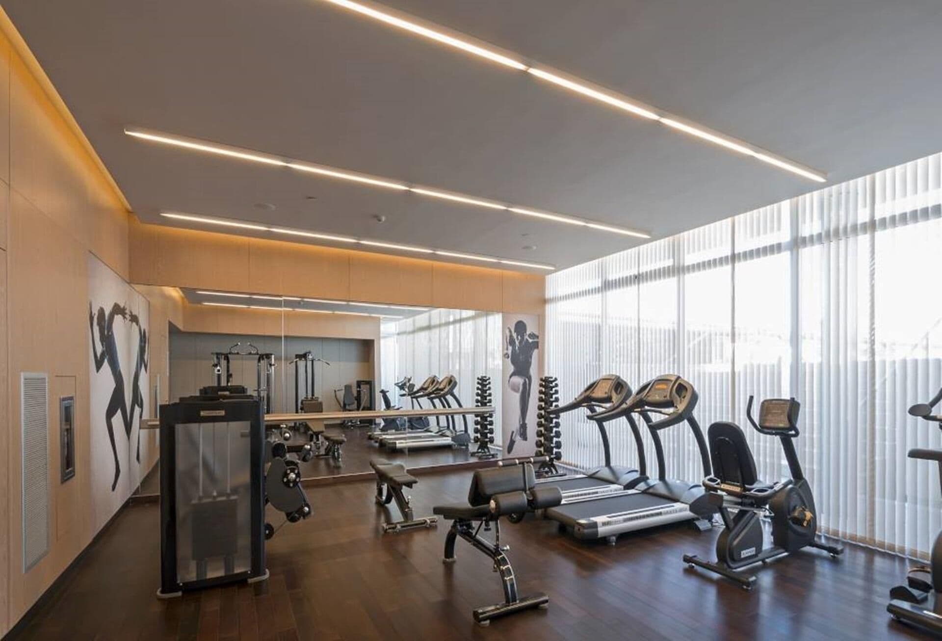 Ein modernes Fitnessstudio mit unterschiedlichen Trainingsgeräten, großen Fenstern und einem klaren, minimalistischen Design.
