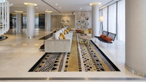 Un lobby amplio con un diseño moderno, que incluye un sofá largo, un banco y una alfombra estampada.