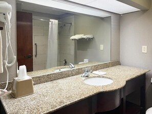 Baño con encimera de granito, lavamanos, espejo, toallero y secador de pelo.