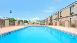 Una piscina con superficie de agua azul cristalina, rodeada por una cerca y contigua a un edificio con múltiples ventanas y balcones.