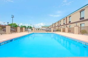 Una piscina con superficie de agua azul cristalina, rodeada por una cerca y contigua a un edificio con múltiples ventanas y balcones.