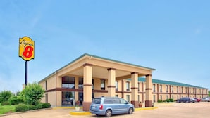 Un hotel Super 8 con una entrada principal cubierta, un estacionamiento y un cielo azul despejado.