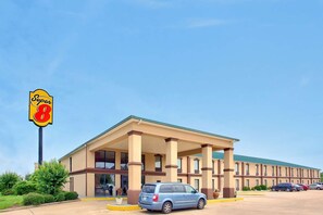 Un hotel Super 8 con una entrada principal cubierta, un estacionamiento y un cielo azul despejado.