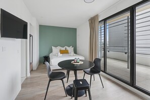Une chambre d’hôtel moderne équipée d’un lit, d’une télévision, d’une table à manger avec des chaises et d’un balcon avec une rambarde.