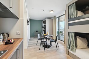 Une cuisine moderne avec un plan de travail en bois, un coin repas avec une table ronde et quatre chaises, et un lit superposé avec des rideaux.