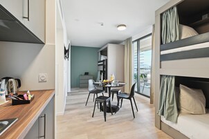 Una cocina moderna con encimera de madera, una zona de comedor con una mesa redonda y cuatro sillas, y una cama litera con cortinas.
