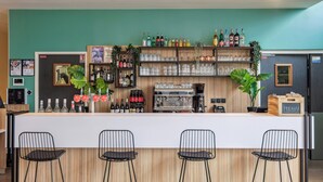 A bar area with a counter, bar stools, shelves with bottles, glasses, and a coffee machine.