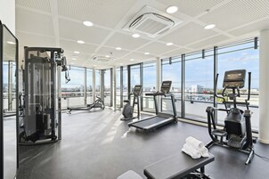 Un gimnasio con equipo de ejercicio diverso, amplios ventanales y vista a la ciudad.
