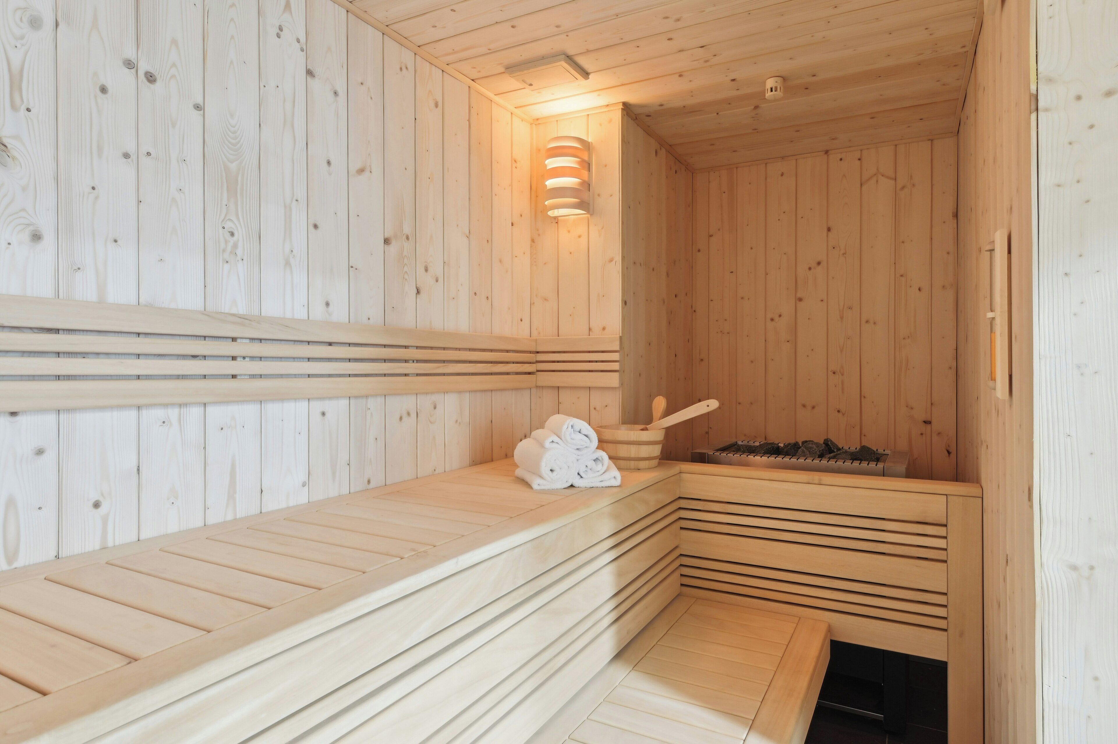 A wooden sauna with benches, a towel stack, and a stone heater.