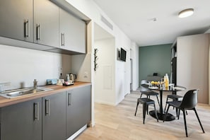 Cocina moderna con armarios grises, encimera de madera y comedor con mesa redonda y sillas negras.