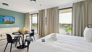A hotel room with a bed, a dining table with chairs, a sofa, and a large window with curtains. - All Suites Appart Hotel Paris Ouest Colombes (Colombes)