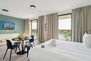 Une chambre d’hôtel comprenant un lit, une table à manger avec des chaises, un canapé et une grande fenêtre avec des rideaux.