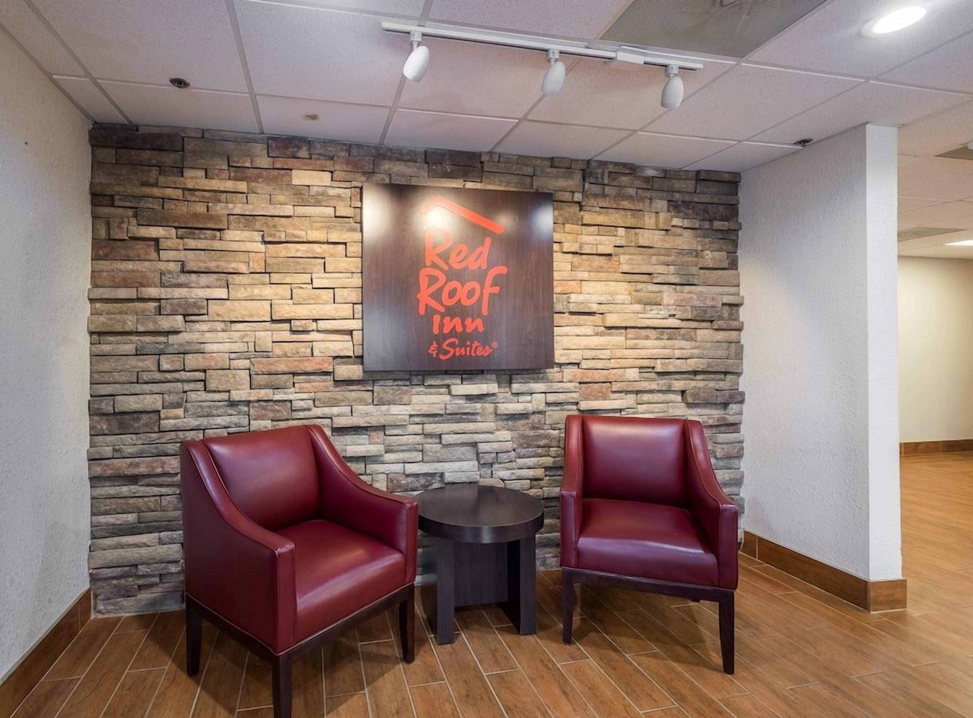 A Red Roof Inn & Suites sign on a stone wall, two red leather chairs, and a small round table.