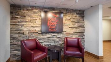 A Red Roof Inn & Suites sign on a stone wall, two red leather chairs, and a small round table.