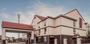 Un Red Roof Inn con una estructura de dos pisos, un área de estacionamiento techada y un cielo despejado.