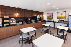 A restaurant with a counter, tables, chairs, and a wall with circular patterns. - Wingate by Wyndham Augusta I-20 (Augusta)