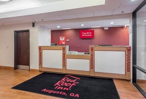 Un área de recepción con un letrero de Red Roof Inn, un aviso de Wi-Fi gratuito y una cámara de seguridad.