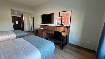 A hotel room with two beds, a desk, a chair, a television, and artwork on the wall.