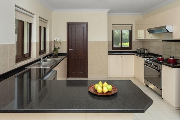 A kitchen with a central island, a stove, and a sink. - Dubai Creek Club Villas (Dubai)