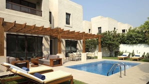 A modern outdoor pool area with lounge chairs, a pergola, and a clear blue pool. - Dubai Creek Club Villas (Dubai)