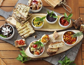 Ein Holzbrett mit verschiedenen Speisen und Brot, darunter Bruschetta, Dips und ein Käsegericht.
