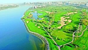 A golf course with a water body, city skyline, and modern buildings in the background. - Dubai Creek Club Villas (Dubai)